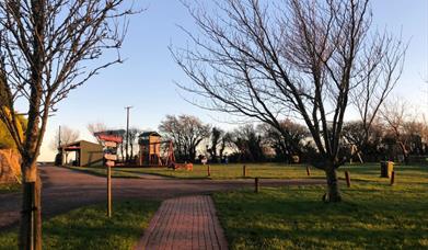 A red brick path leading to an outdoor park. Trees are in the foreground and golden light covers the area.