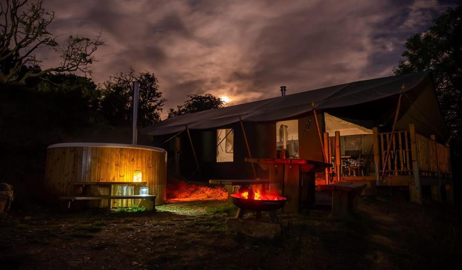 Safari tent at night with wood fired hot tub in the foreground