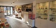 gallery shop inside view toward an entrance door. There are glass shelves on the right with jewelry inside and white plinths with books and cards of t