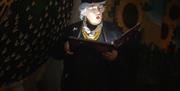 Alison reading from book in dimly lit room