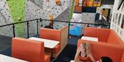 Two ladies sit on padded seats at a table in a café area on a balcony overlooking a huge part of the climbing walls.