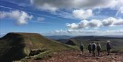 Five people walking into the distance on top of a ridge, facing a peak with blue skies and fluffy clouds