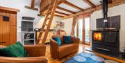 A leather sofa and chair sit behind a blue rug next to an Esse wood burner stove, French doors lead to outside and an oak ladder lead up into the oak