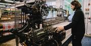 A craftsperson dressed in black is weaving flannel on a loom.