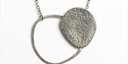 Silver necklace with chain attached to  a silver circular form with a filled circular form attached to one side.