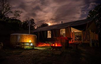 Safari tent at night with wood fired hot tub in the foreground