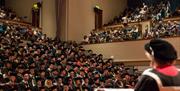 A busy auditorium of graduating students dressed in robes.