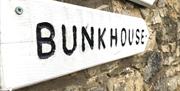 A white wooden sign on a stone wall with the words 'Bunkhouse' engraved and painted black.
