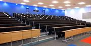 Empty lecture room with rows of seats and desks facing a screen.